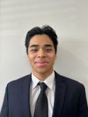 A young tan asian man with short dark brown hair wears a navy blue suit jacket and tie on top of a white collared shirt and smiles at the camera. 